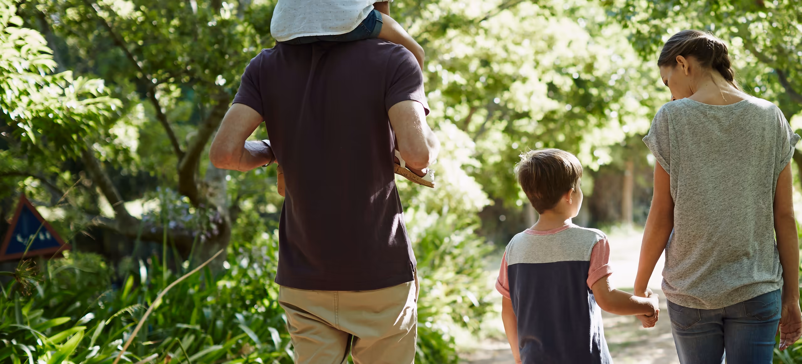 A family walking away down a leafy path, one child on a parent’s shoulders