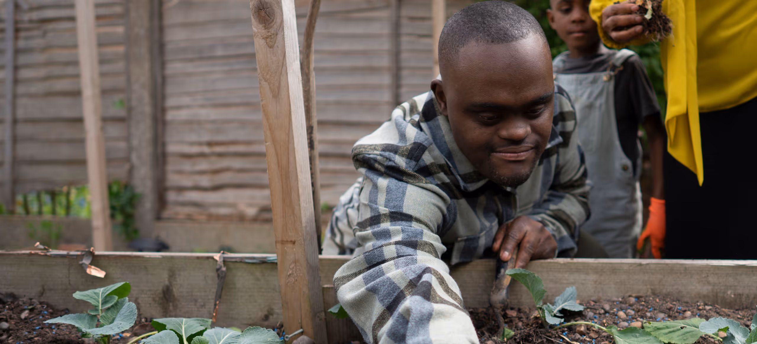 A man planting seedlings in a raised garden bed while family members work nearby