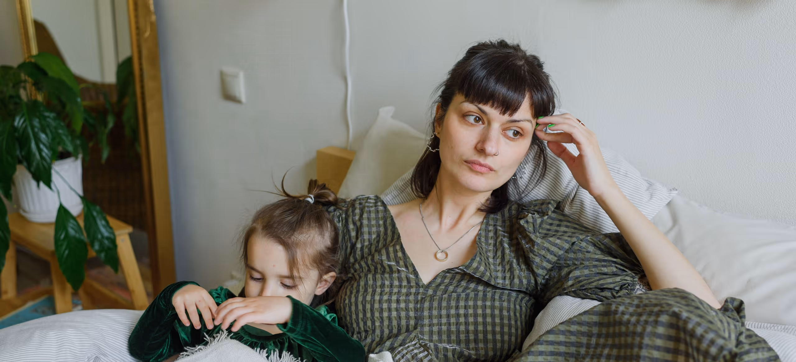 A parent lying on a bed looking away while a young child sleeps beside her