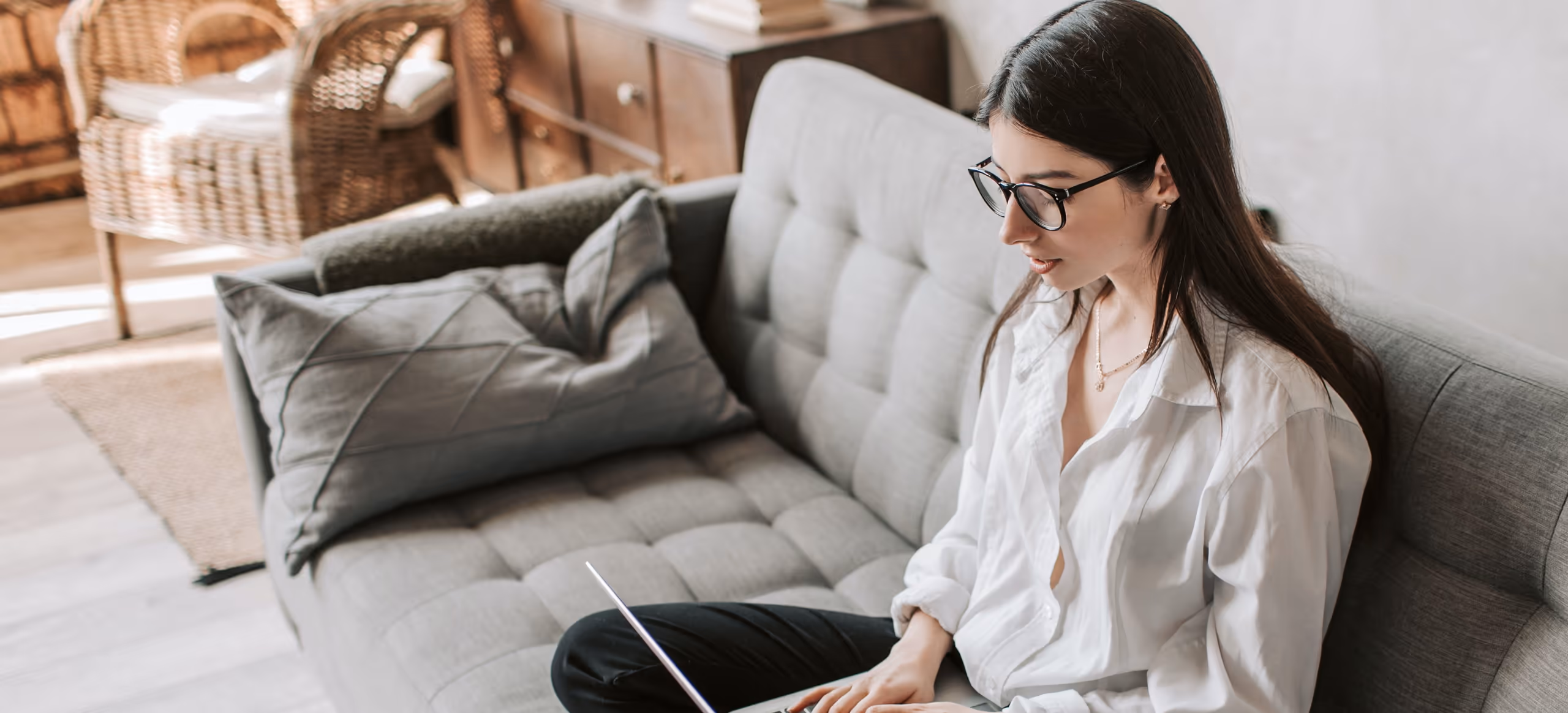 A woman sitting cross-legged on a couch at home, working on a laptop