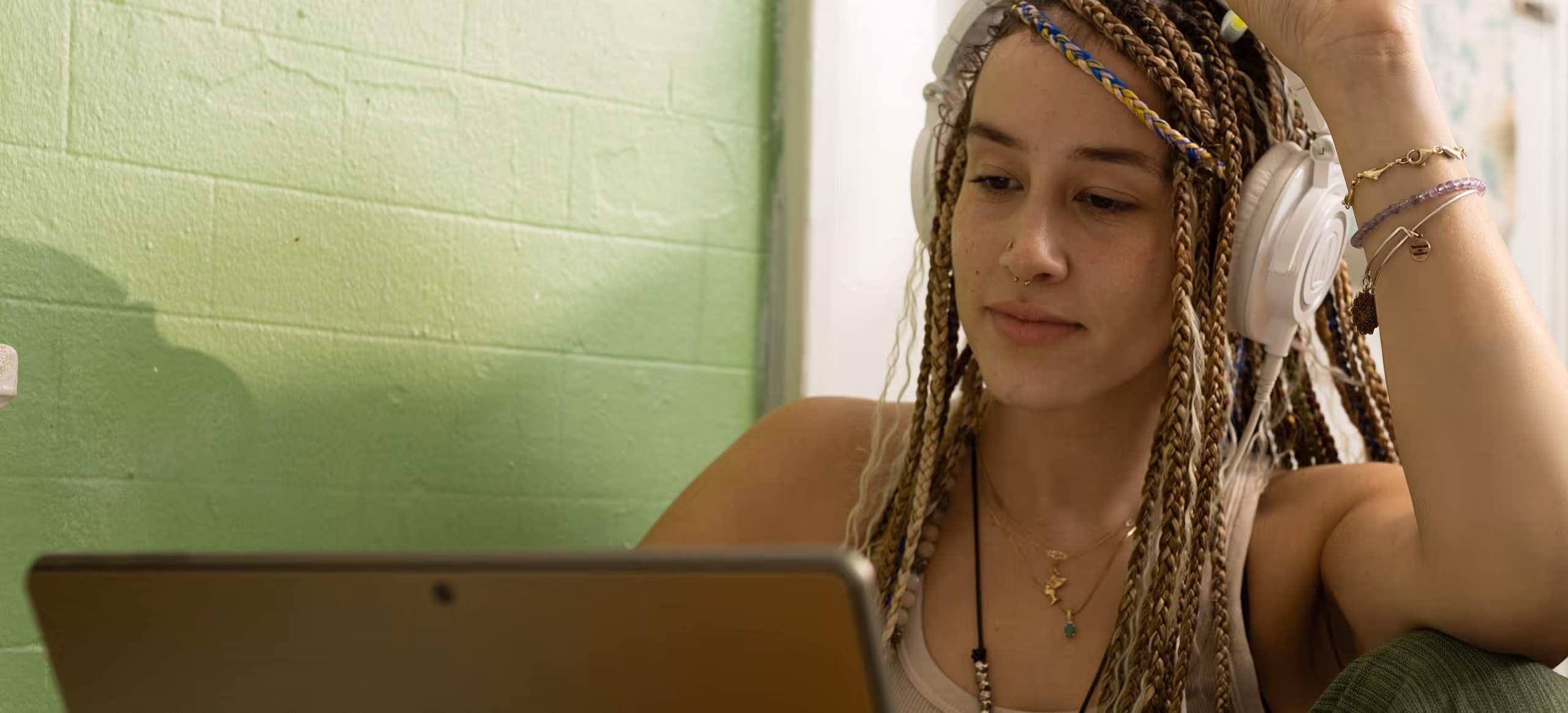 A young woman in headphones at a kitchen table, watching a tablet